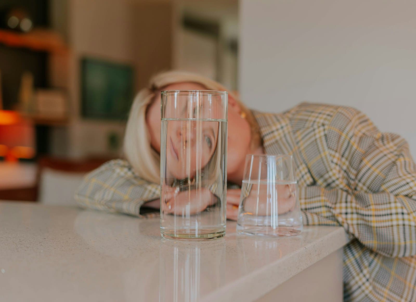 a woman laying her head on a counter next to a glass of water, the reflection makes her face look backwards. A weed hangover can leave you feeling scrambled too.
