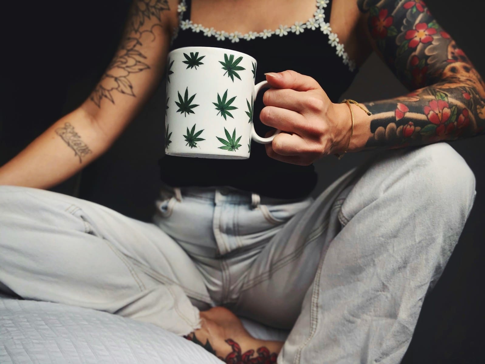 woman in white and black floral spaghetti strap top and gray pants holding white and green marijuana leaf printed mug.